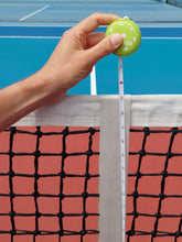 Load image into Gallery viewer, Hand holding a green round net checker tape measure against a pickleball net.